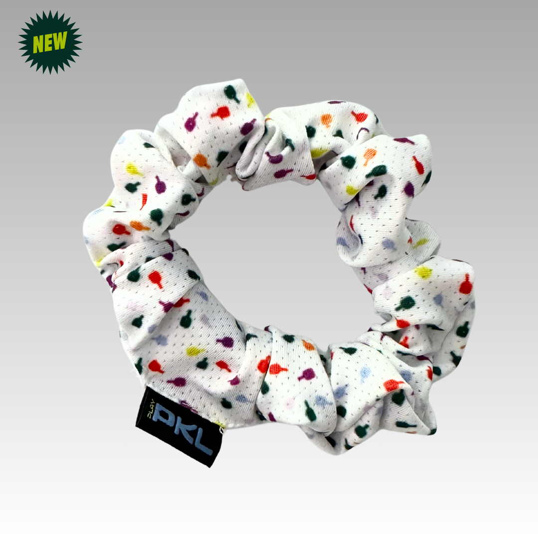 The Shanti Pickleball Hair Scrunchie by Playly Store is white with a colorful paint-splatter pattern and a small black PKL tag, shown on a gray gradient background with a green NEW badge in the top left corner.