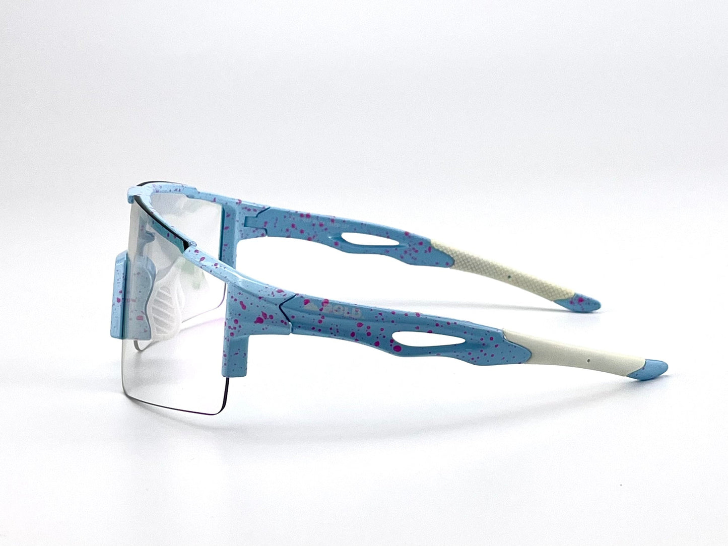 The BOLD Wavelength Performance Sunglasses by boldouterwear are sporty, semi-rimless blue shades with white arms, pink splatter details, beige accents, and textured tips. Ideal for trail running, they are shown facing left against a plain white backdrop.