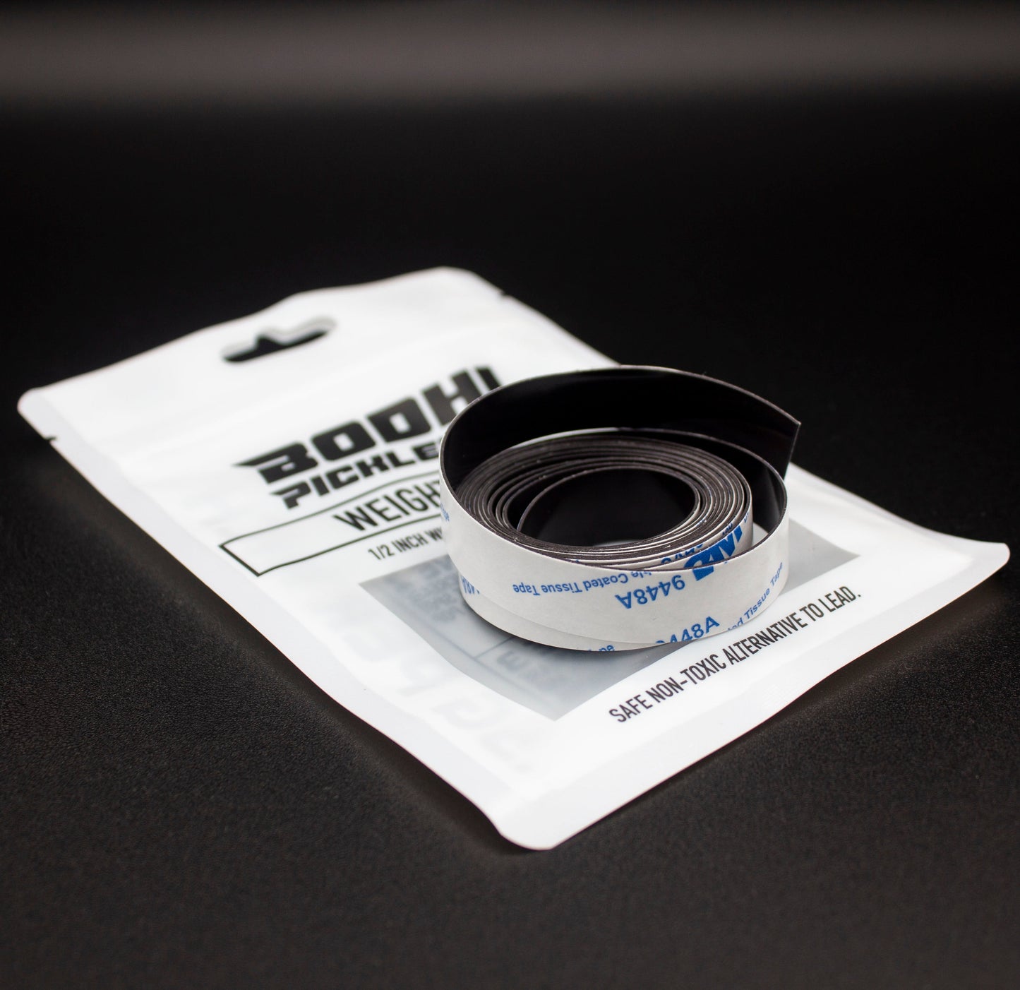 A coiled strip of PROtune™ Weighted Tape rests on a white Bodhi Performance package. The tape’s adhesive backing is partly exposed, and the blue packaging emphasizes paddle customization and safety features.