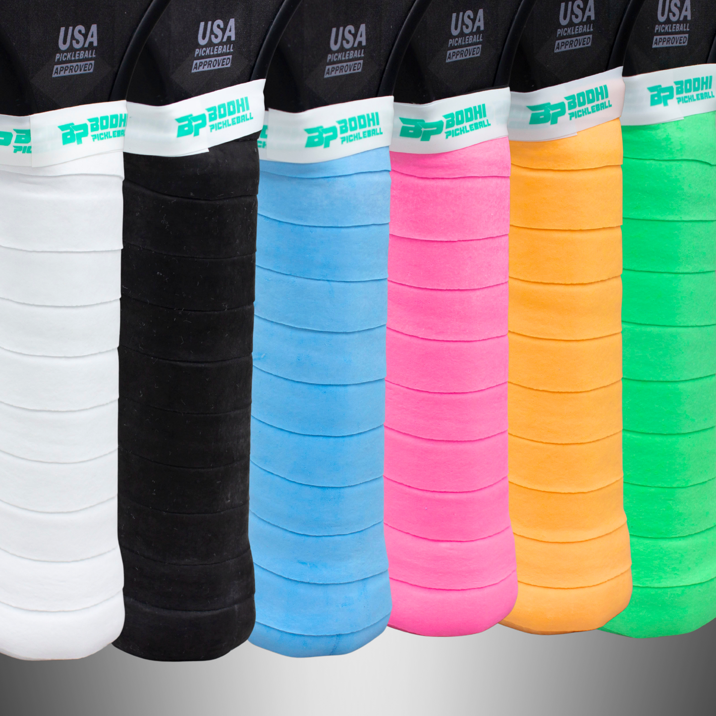 Six DRYtack™ Premium Pickleball Overgrips by Bodhi Performance stand upright in assorted colors. These cushioned grips offer moisture control and display "USA Pickleball Approved" at the paddle tops.
