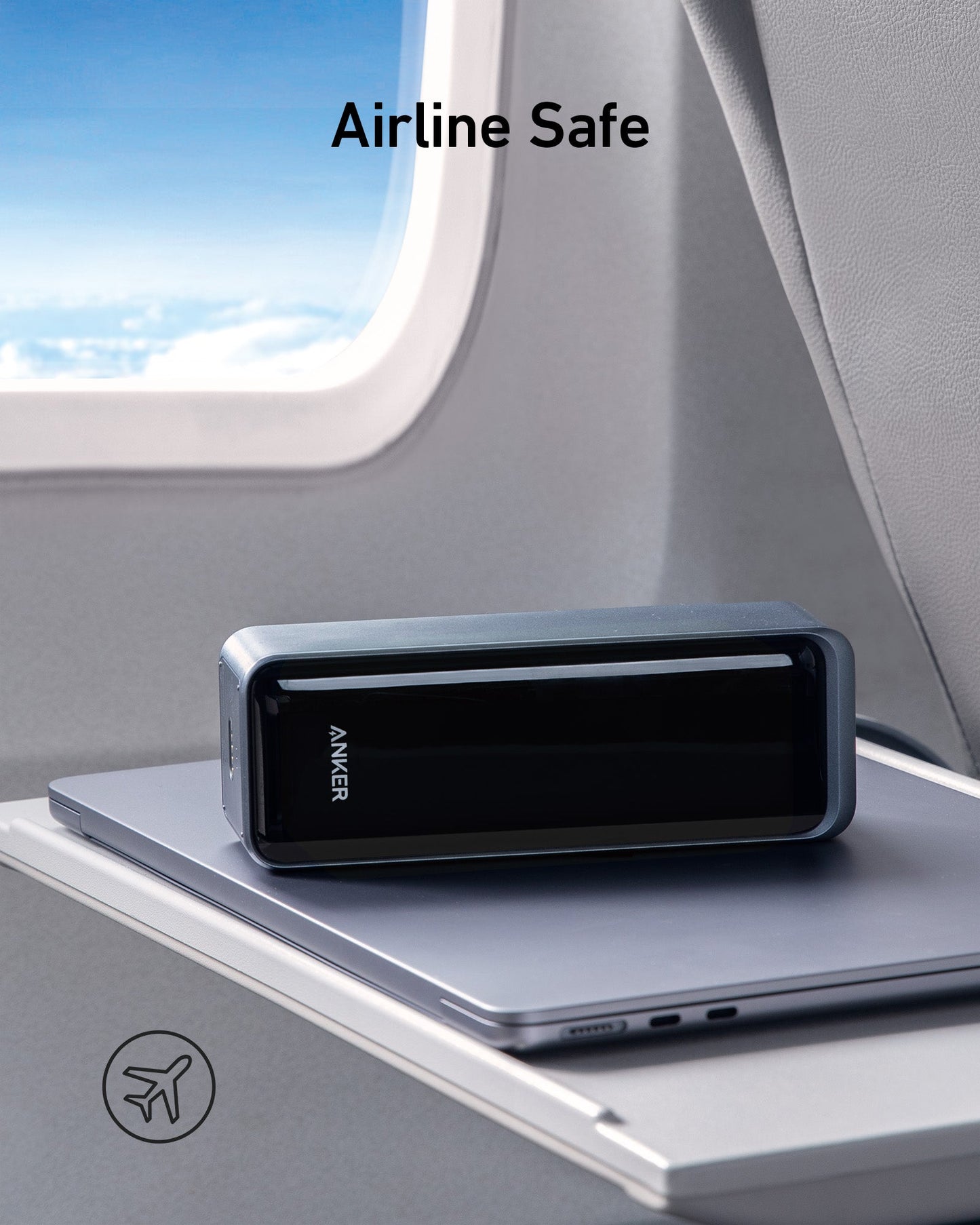 An Anker Prime 27,650mAh Power Bank (250W) and 100W Charging Base sits on a closed laptop atop an airplane tray. "Airline Safe" is displayed above, with an airplane icon on the lower left. Blue sky and clouds are visible through the window.
