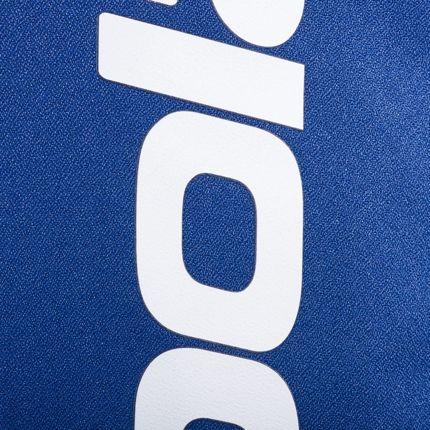 Close-up of bold white lowercase letters on a textured blue background, likely part of the Babolat COURT Backpack LITE by Padel USA. The vertically oriented text suggests recycled materials used in its design.