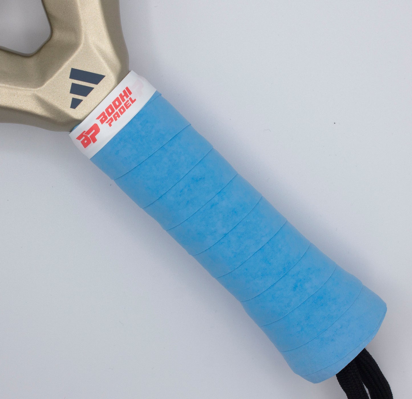 Close-up of a Bodhi Performance DRYtack™ Premium Padel Overgrip in bright blue, wrapped on a racket handle. The top is finished with a white band featuring red and black logos, plus part of the beige frame and a black wrist strap are visible.
