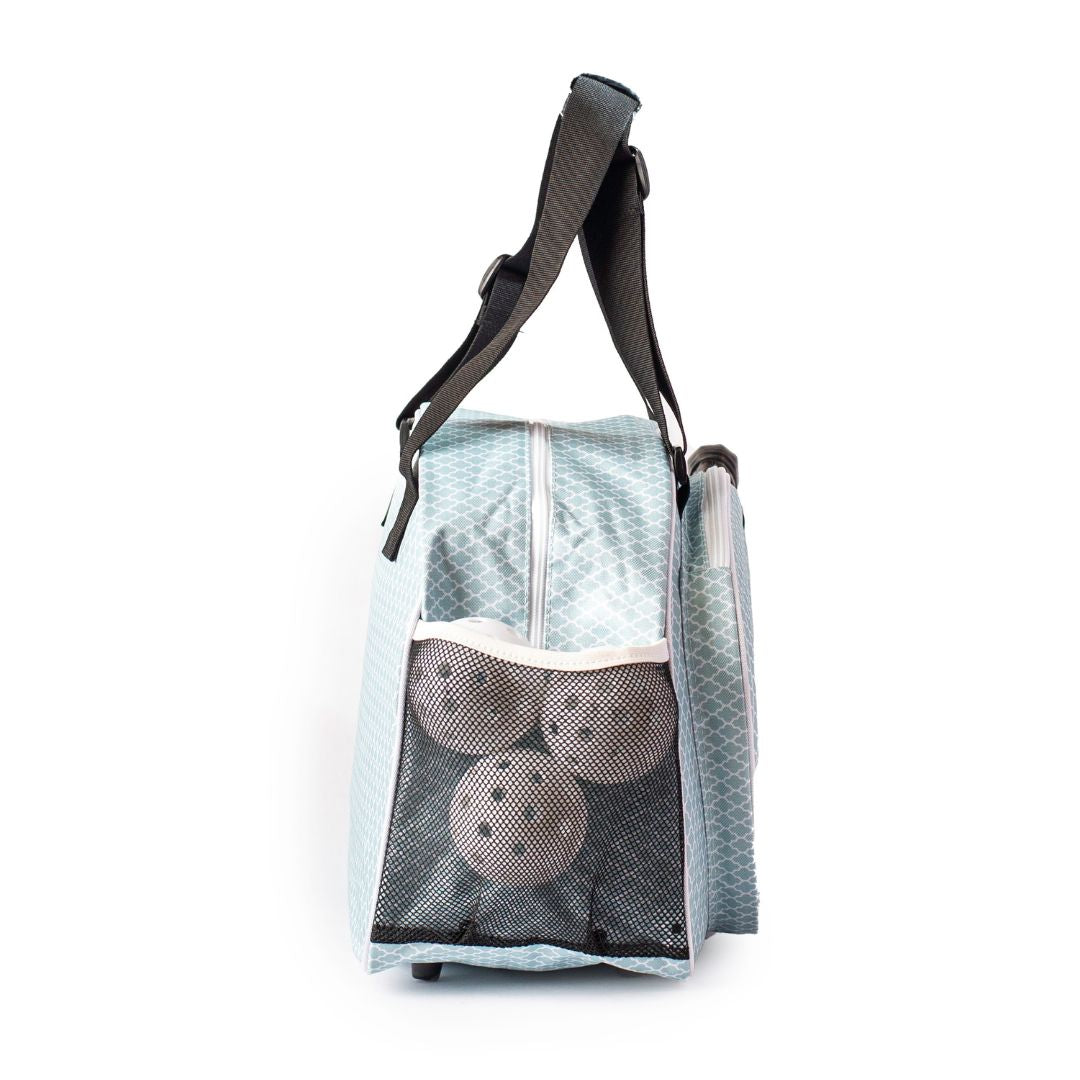The Classy Sage Premium Women's Pickleball Bag by Pik'le'Ball Sports is shown from the side, featuring a black shoulder strap, white zipper, mesh pocket with three brown balls, and subtle geometric pattern against a white background.