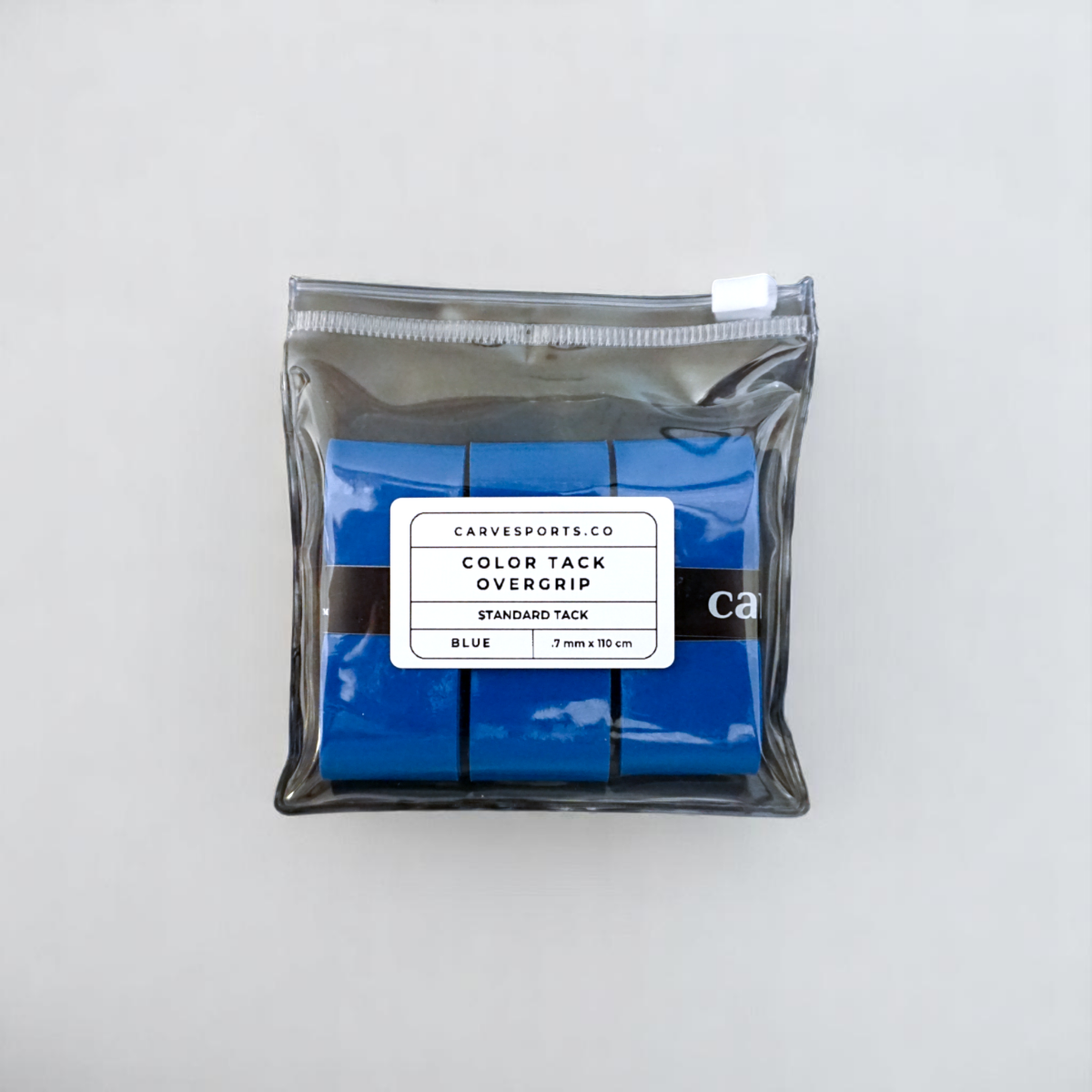 A clear pouch from Carve Sports holds three blue Color Overgrips, each with a high-tack surface. The label says “Color Overgrip, Standard Tack, Blue, 3mm x 110cm.” The pouch is set against a plain light background.