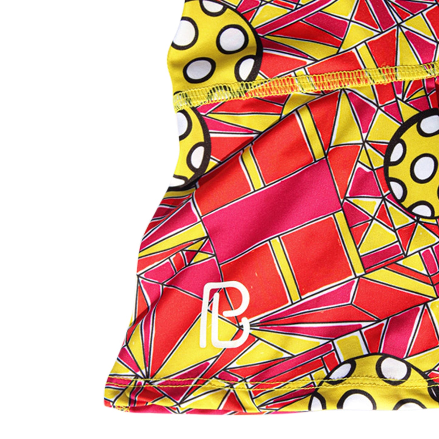 The Pickleball Bella PB Drop Pleat Skort features a close-up of its vibrant geometric pattern in red, orange, and yellow with black outlines. Large yellow circles with white dots and a white stylized PB logo on the lower left complete the design.