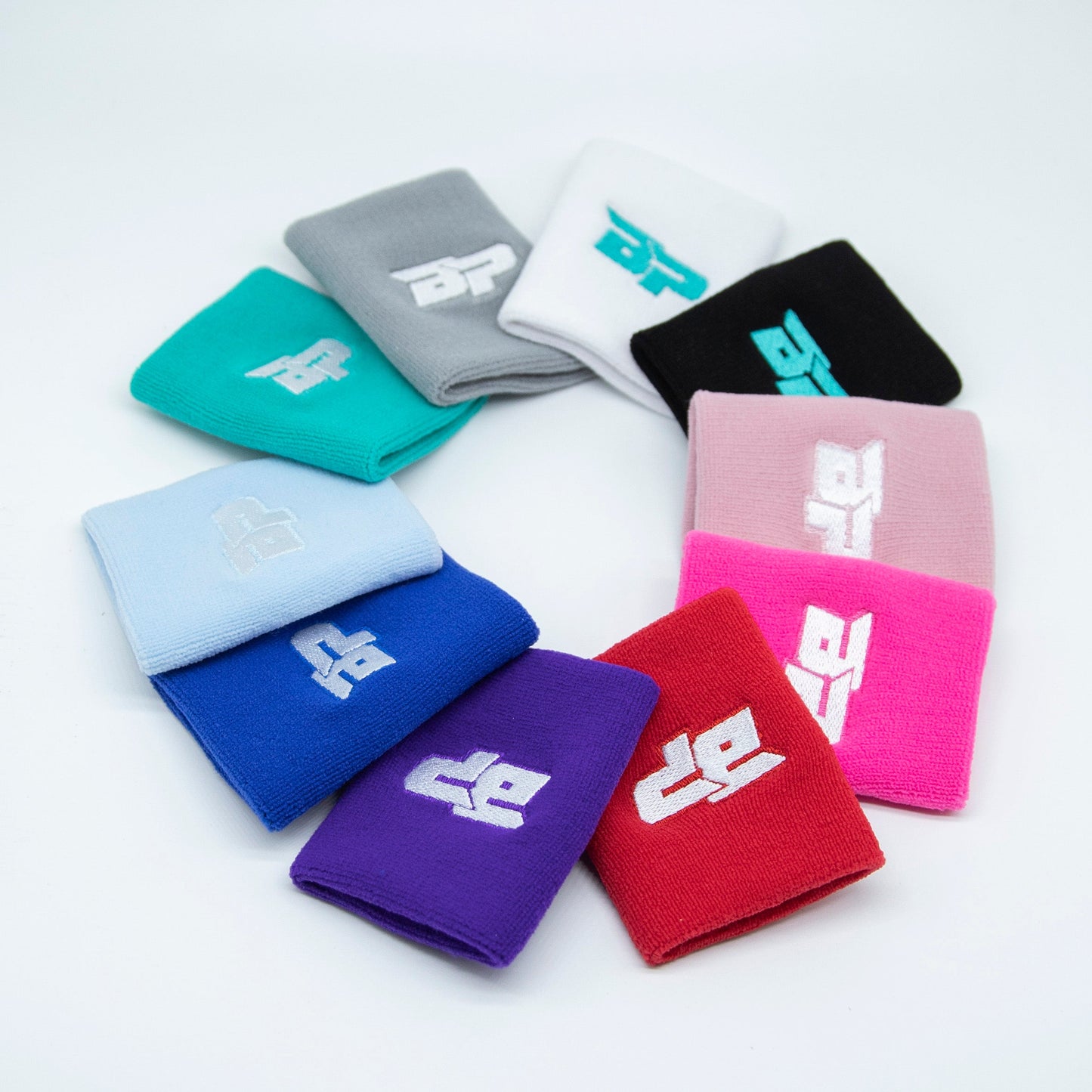 A circular display of ten colorful Bodhi Performance Wristbands (1pc), each with a white stylized logo. Available in teal, gray, black, pink, red, purple, blue and more—ideal as a sweat-wicking or pickleball wristband.