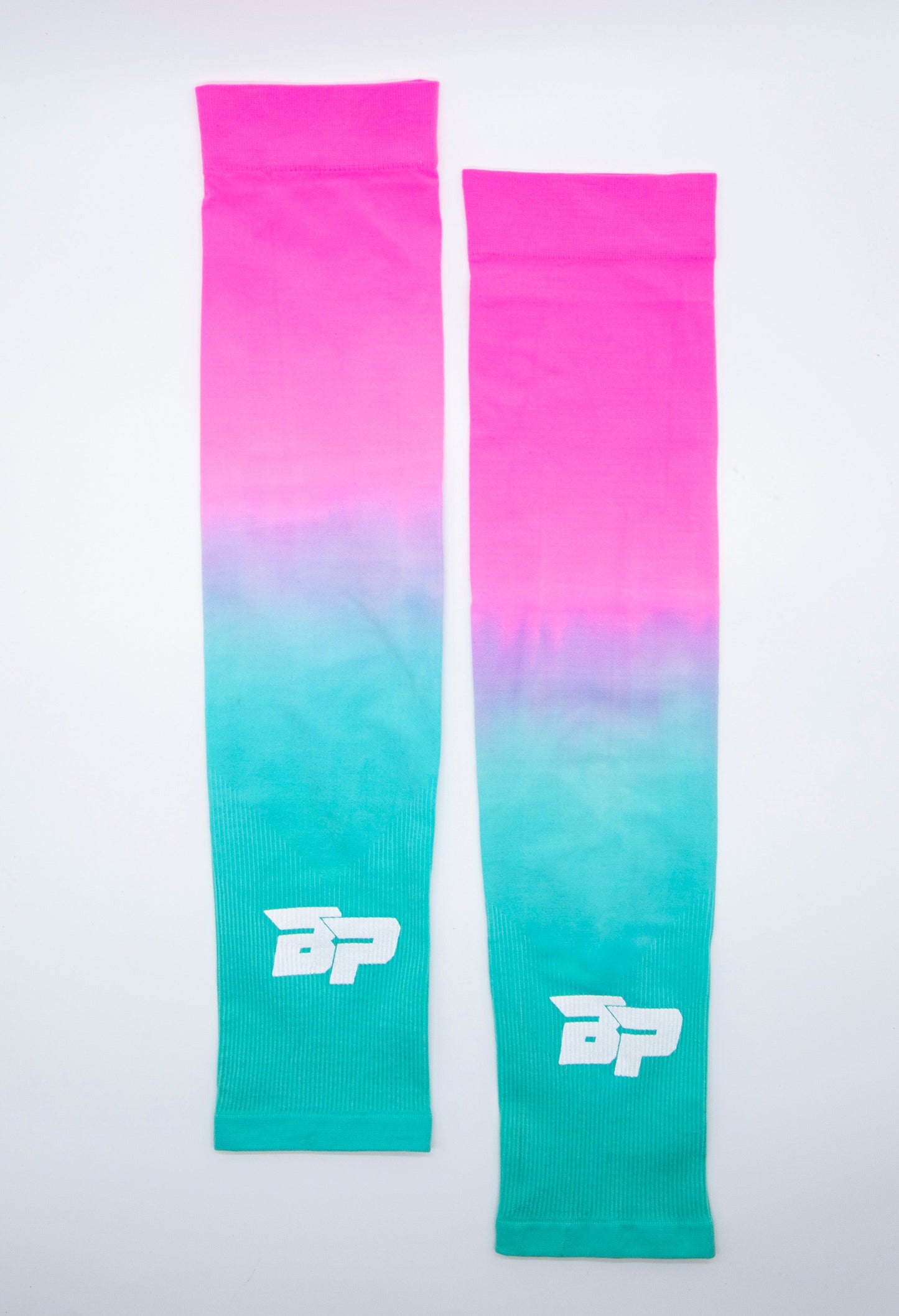 Two Bodhi Performance Arm Sleeves are laid flat side by side on a white background. They feature a bright pink to turquoise gradient and display a white stylized BP logo near the wrist, combining style and function for athletic performance.