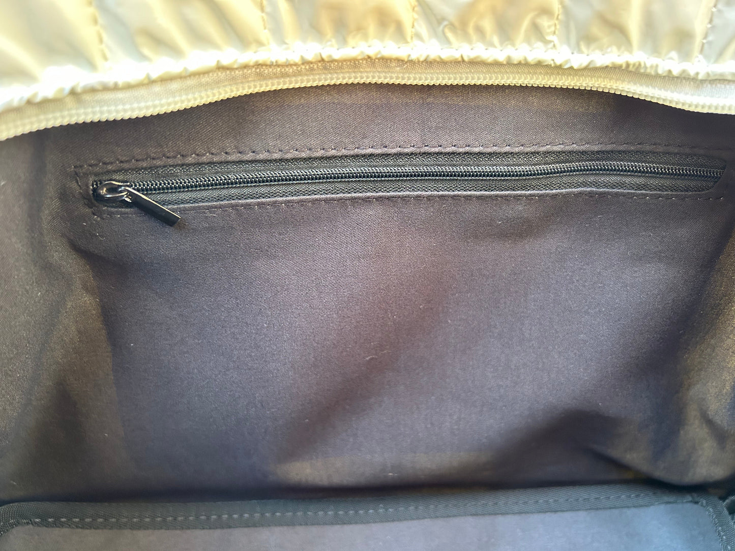 Close-up of the inside of Runway Athletics' Quilted Puffer Pickleball Tote in White, featuring a black zippered inner pocket with a small pull tab and an upper edge lined with light-colored or metallic material.