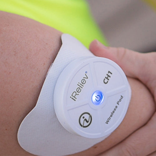 An iReliev Wireless Large Single Pad from the Refill Kit, with a glowing blue power button, is attached to a person's upper arm using iReliev’s hydrogel multi-layer adhesive pad for pain relief therapy as their hand gently touches their arm.