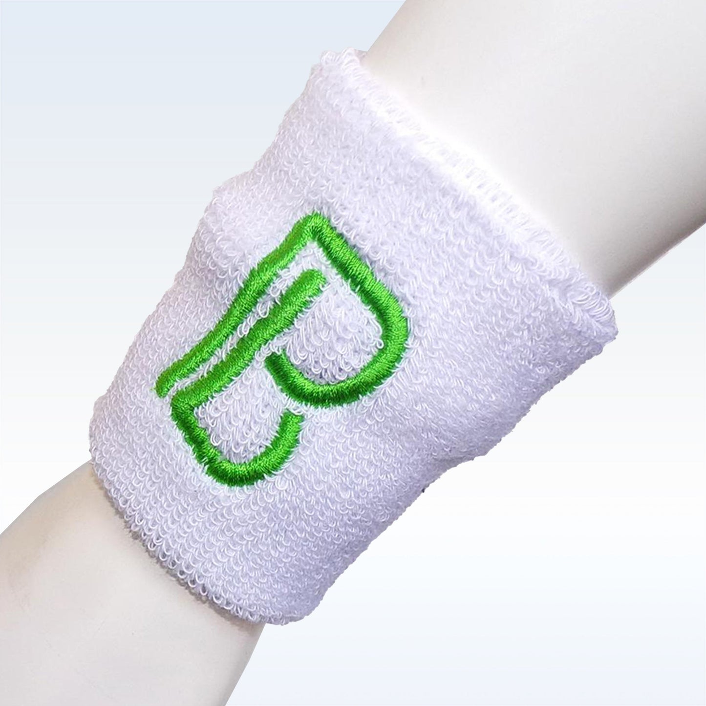 A Pickleball Bella Wristband—a soft, absorbent white terry cloth band with a green embroidered B—stands out against a blue-to-white gradient background, making it the perfect pickleball wrist accessory from Pickleball Bella.