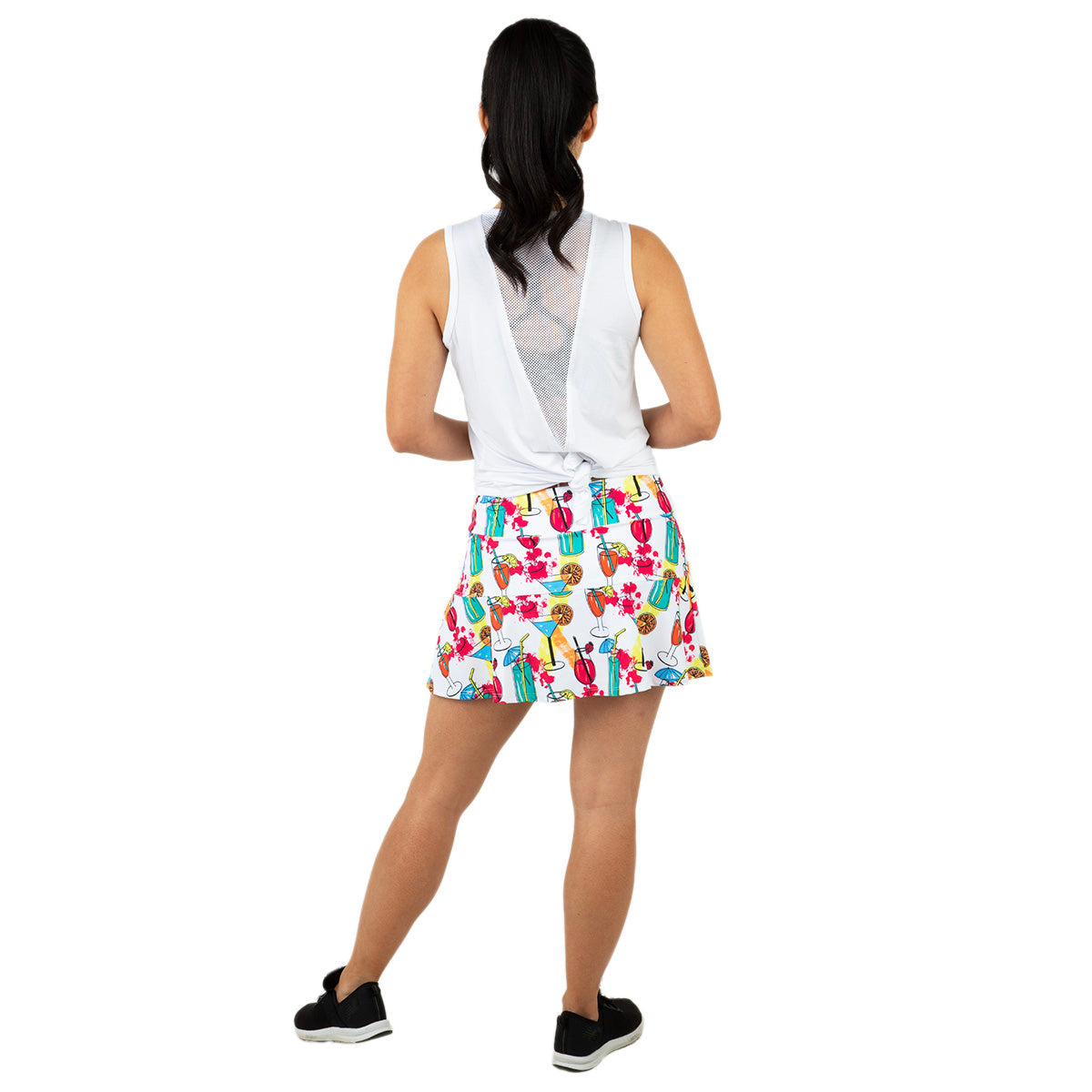 A woman with a ponytail models the Queen of the Court Cocktails on the Court Swing Skirt, featuring a colorful cartoon cactus print, paired with a white sleeveless top and black sneakers, standing against a plain white background.