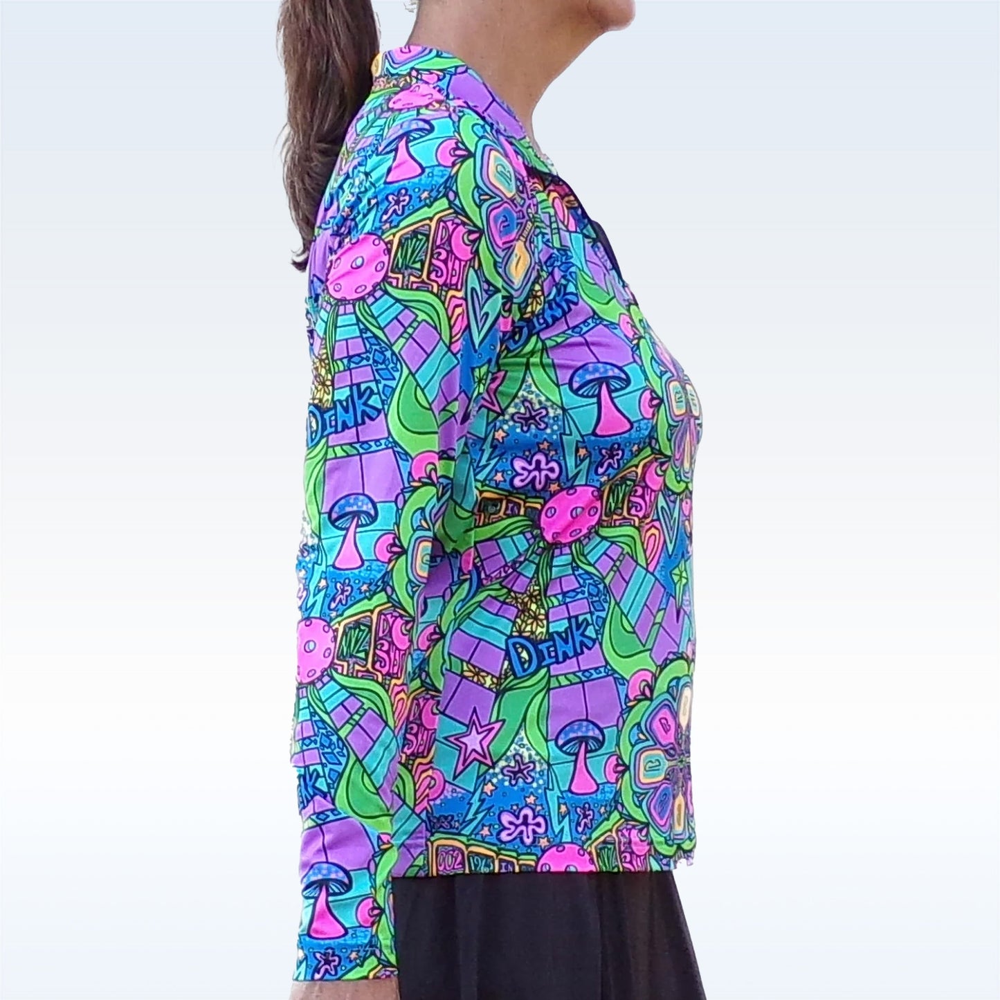 A person with long dark hair in a ponytail wears the Pickleball Bella PB 1/4 Zip Long Sleeve Groovy top, featuring a psychedelic pattern with mushrooms, stars, flowers, and "DINK"—a stylish pickleball shirt with UV protection.