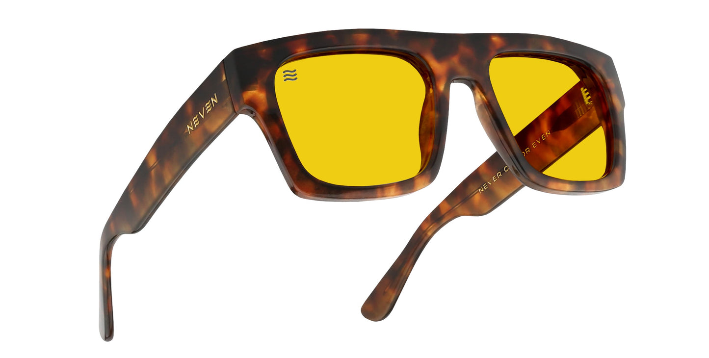 A pair of chunky, square tortoise shell sunglasses—Amar by Neven Eyewear—with yellow-tinted lenses. The left arm is printed with “Neven Eyewear” in gold, and slightly curved arms complete this bold fashion statement.
