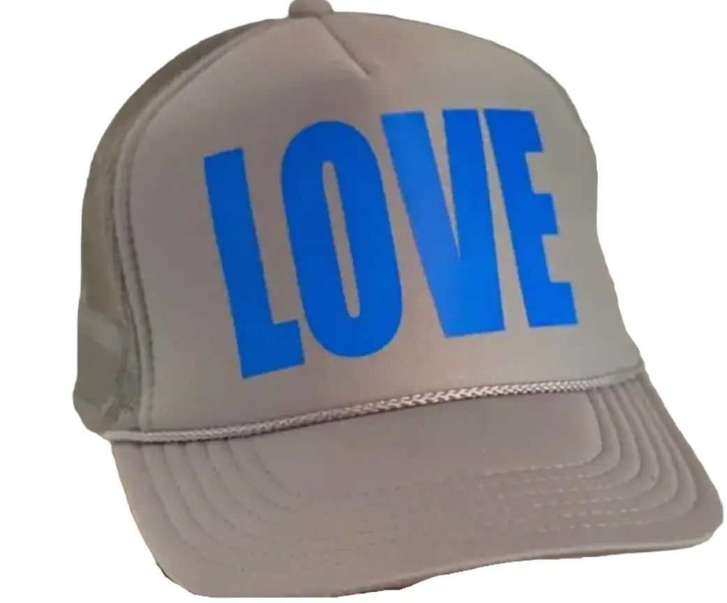 The LOVE Trucker Hat - Soft Grey by Runway Athletics features a curved brim, breathable mesh back, and bold bright blue "LOVE" lettering on the front panel. The hat is shown angled to highlight the front and part of the left side.