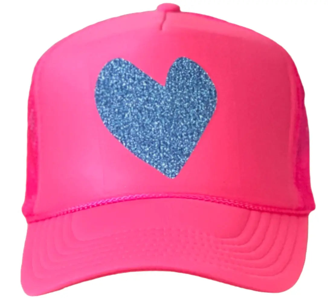 The Heart Trucker Hat - Pink by Runway Athletics features a bold pink design, sparkly blue heart graphic, curved brim, mesh sides for comfort, and neon blue glitter lettering for standout style.