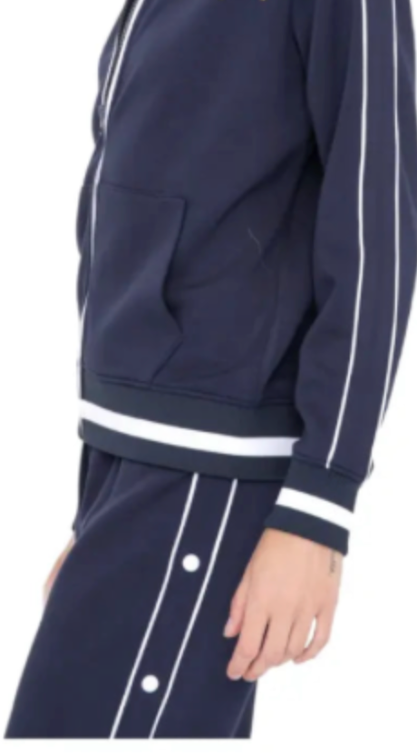 Wearing the Runway Athletics Retro Vibe Tennis Tracksuit - Navy, which features white vertical stripes, white waist trim, side buttons, and a jacket with a front pocket, their hand rests relaxed at their side.