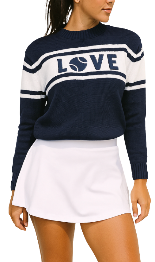 A woman wears the Runway Athletics LOVE Sweater - Navy, featuring white stripes and a tennis ball "O" in an acrylic weave, paired with a white tennis skirt. She stands relaxed, turned slightly to the side against a white background.