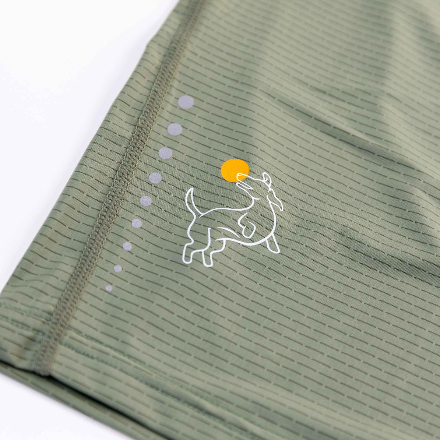 The Women's Dinker LUX Performance Shirt by Swinton Pickleball features light olive green fabric with thin dark lines, neat stitching, and a white dog chasing an orange ball graphic accented by five small curved grey dots.