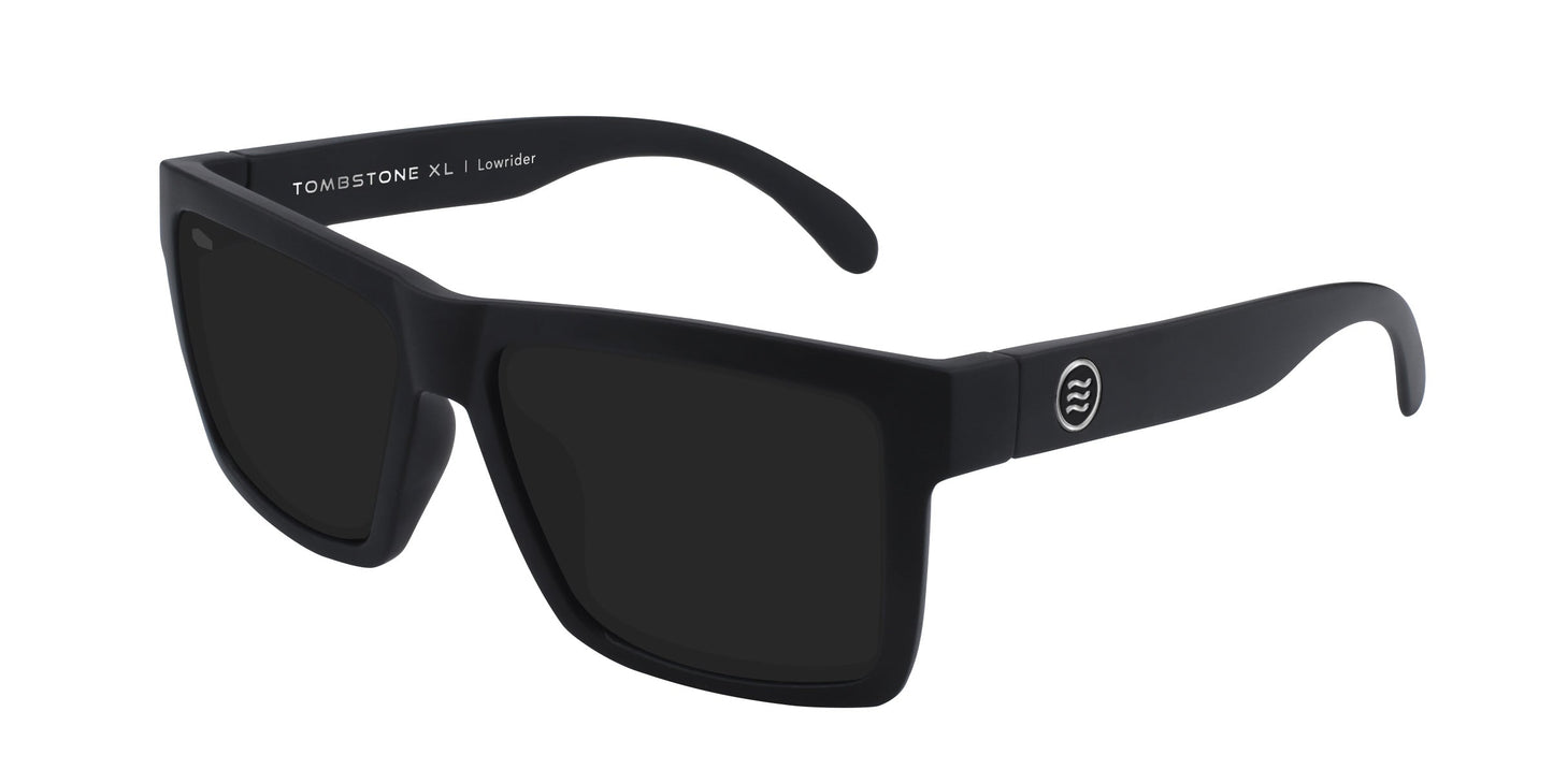 A pair of Neven Eyewear Lowrider XL sunglasses in matte black with dark lenses. The left temple shows TOMBSTONE XL L Ravinder in white; the right arm has a circular logo with three wavy white lines.