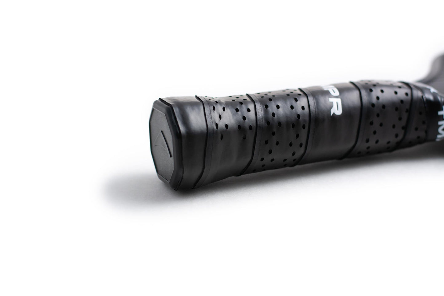 Close-up of the Tantrum XT pickleball paddle handle by TMPR Sports, wrapped in perforated black grip tape. A hexagonal end cap with a subtle triangular logo and a minimal white background highlight its power core design.