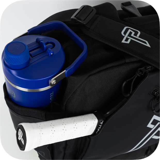 A close-up of the Titan Duffle Bag by Titan Pickleball, a premium black sports bag with white logos, featuring a blue water bottle in the side pocket, a tennis racquet with white grip handle, and adjustable black straps with plastic buckle.