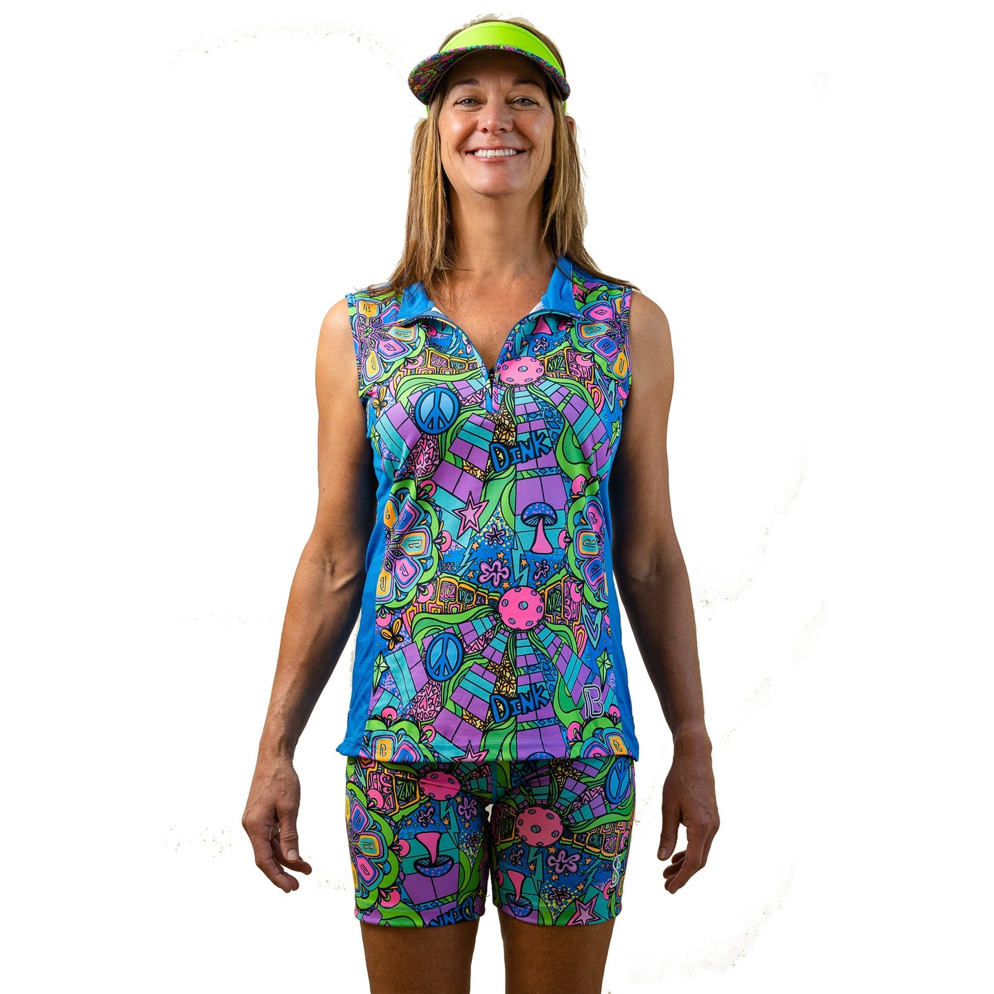 A woman smiles wearing the Pickleball Bella PB 1/4 Zip Sleeveless Groovy top—vibrant with peace signs, flowers, mushrooms, and “ONE”—offering both style and UV protection.