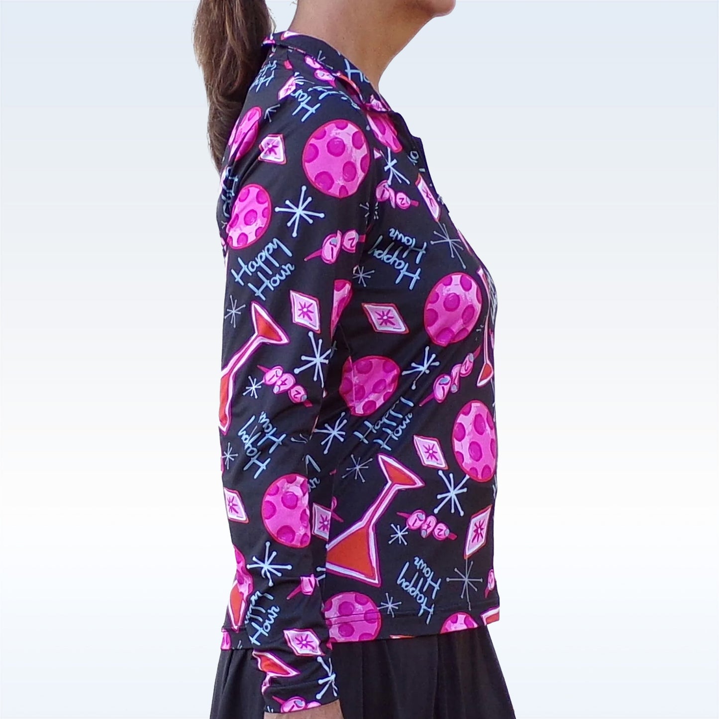 A woman models the Pickleball Bella PB 1/4 Zip Long Sleeve Martini 2-4-1 Happy Hour top, featuring a vibrant pink martini glass pattern, SPF 50+ UV protection, and "happy hour!" in white script on black. Light gray background.