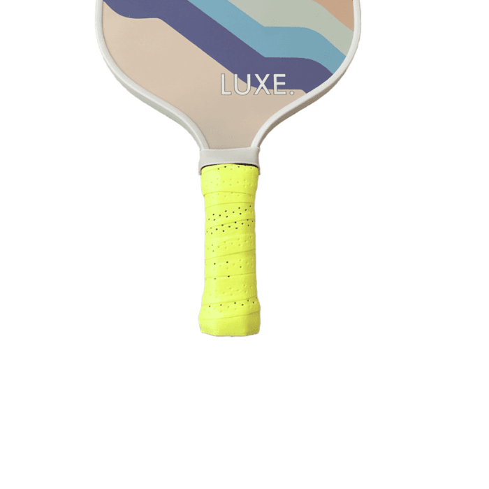 A LUXE Pickleball paddle with "LUXE" near the handle top, diagonal tan, blue, and teal stripes on the face, and a bright yellow perforated Pickleball Paddle Grip for comfort. The background is white.