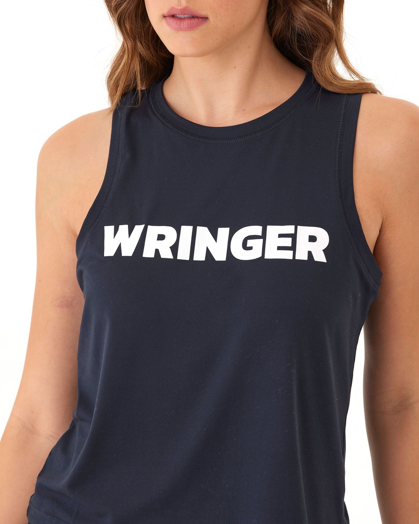 A woman with wavy brown hair wears the Women's Performance Wringer Tank by Wringer Wear, a sleeveless dark navy top with "WRINGER" in bold white letters. The cropped photo shows her from lips to waist against a plain white background.