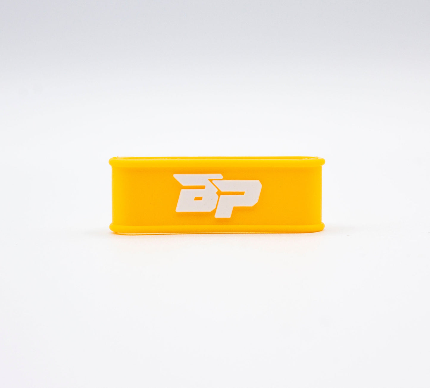 A yellow Bodhi Performance Paddle Band with rounded edges rests on a white surface. The silicone grip band, perfect for pickleball paddles, displays a bold white "BP" logo at the center against an uncluttered background.