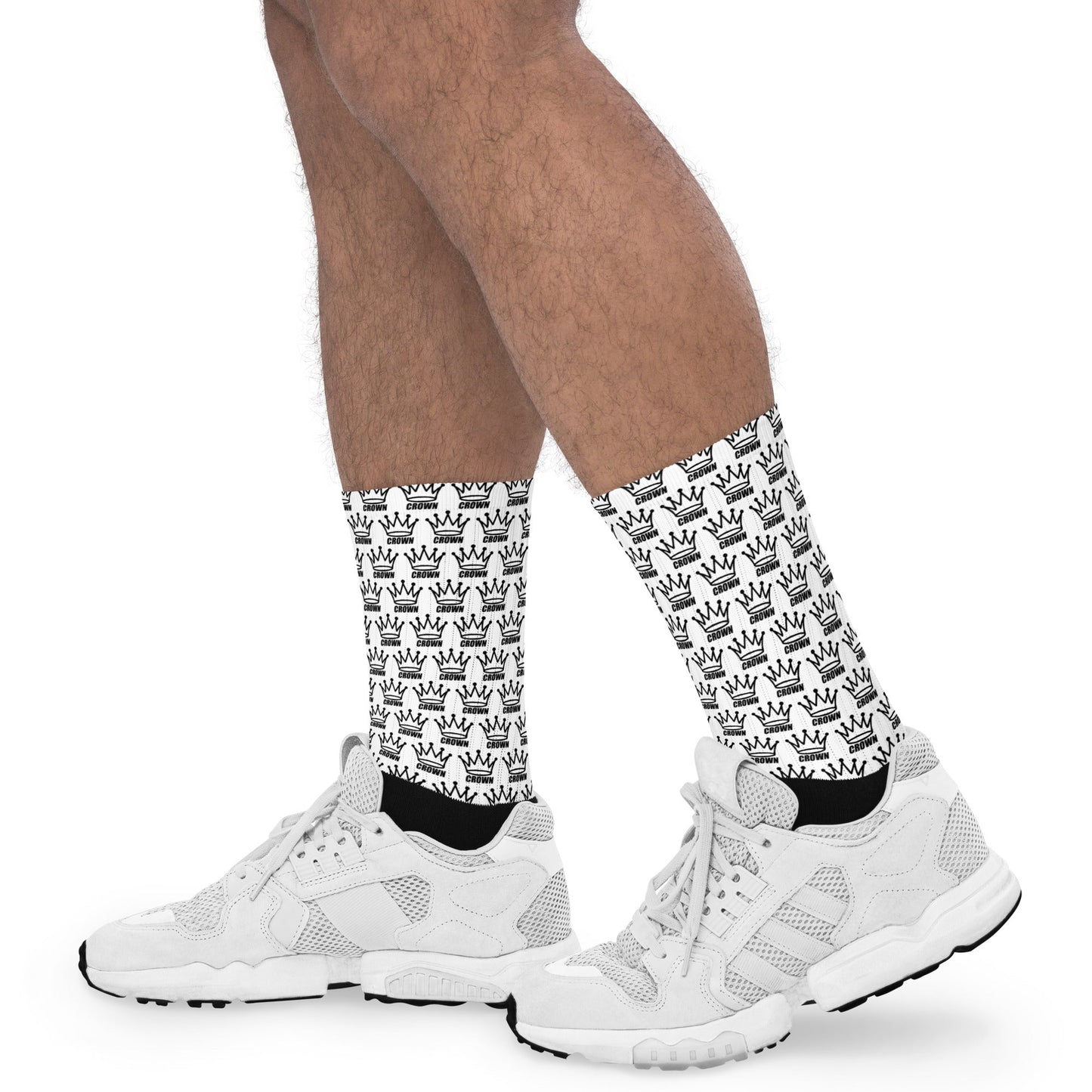 A person wears white athletic shoes and Crown Pickleball crew socks—Checkered Crown (White)—patterned with black crowns. These cushioned socks cover the lower legs and feet, shown against a plain white background.