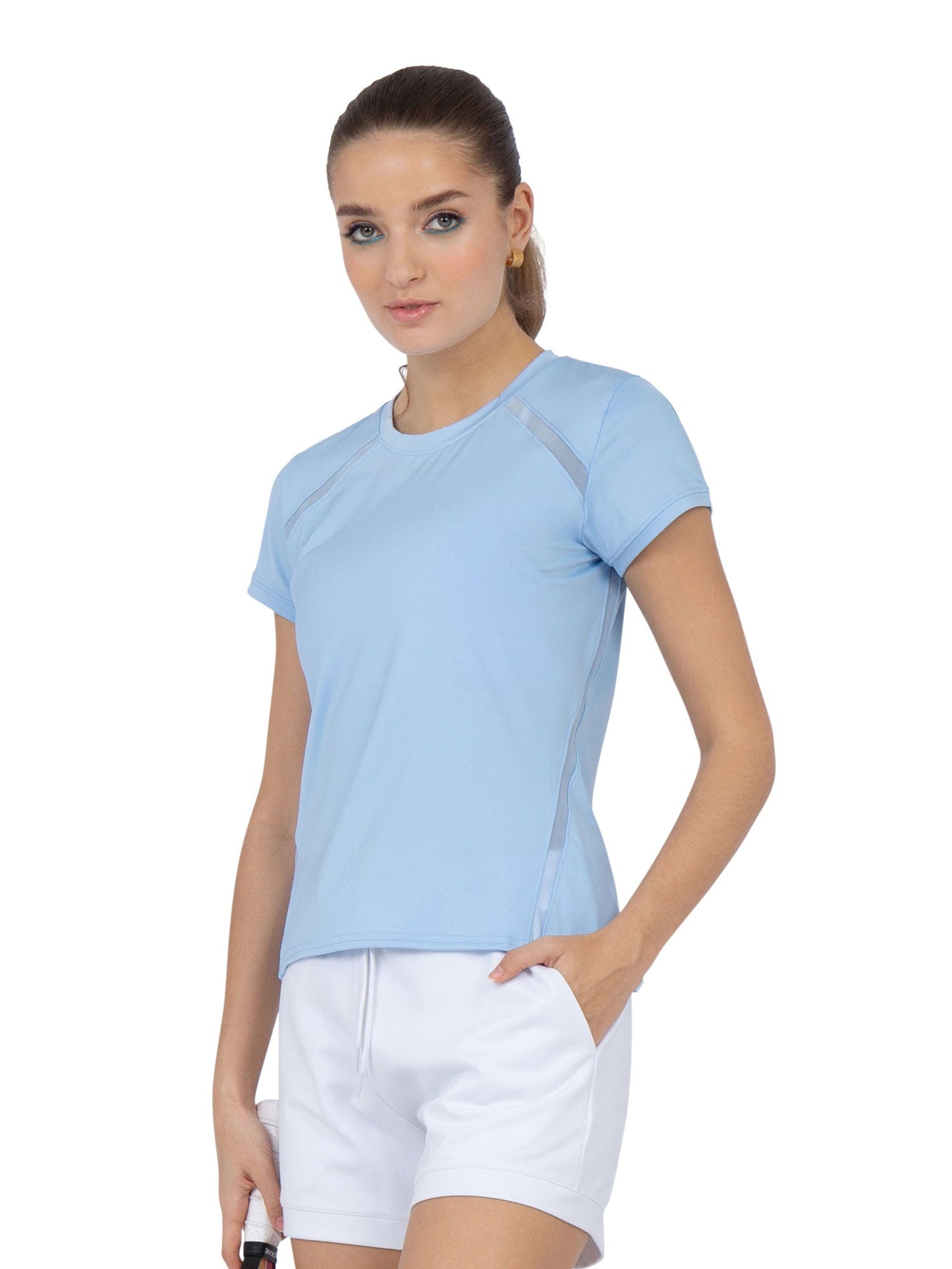 A woman with light skin and blue eyes wears the inPhorm NYC Classic Short Sleeve Crew Neck in Bluebell and white shorts. The moisture-wicking athletic shirt is perfect for staying cool. She poses against a plain white background, looking at the camera.