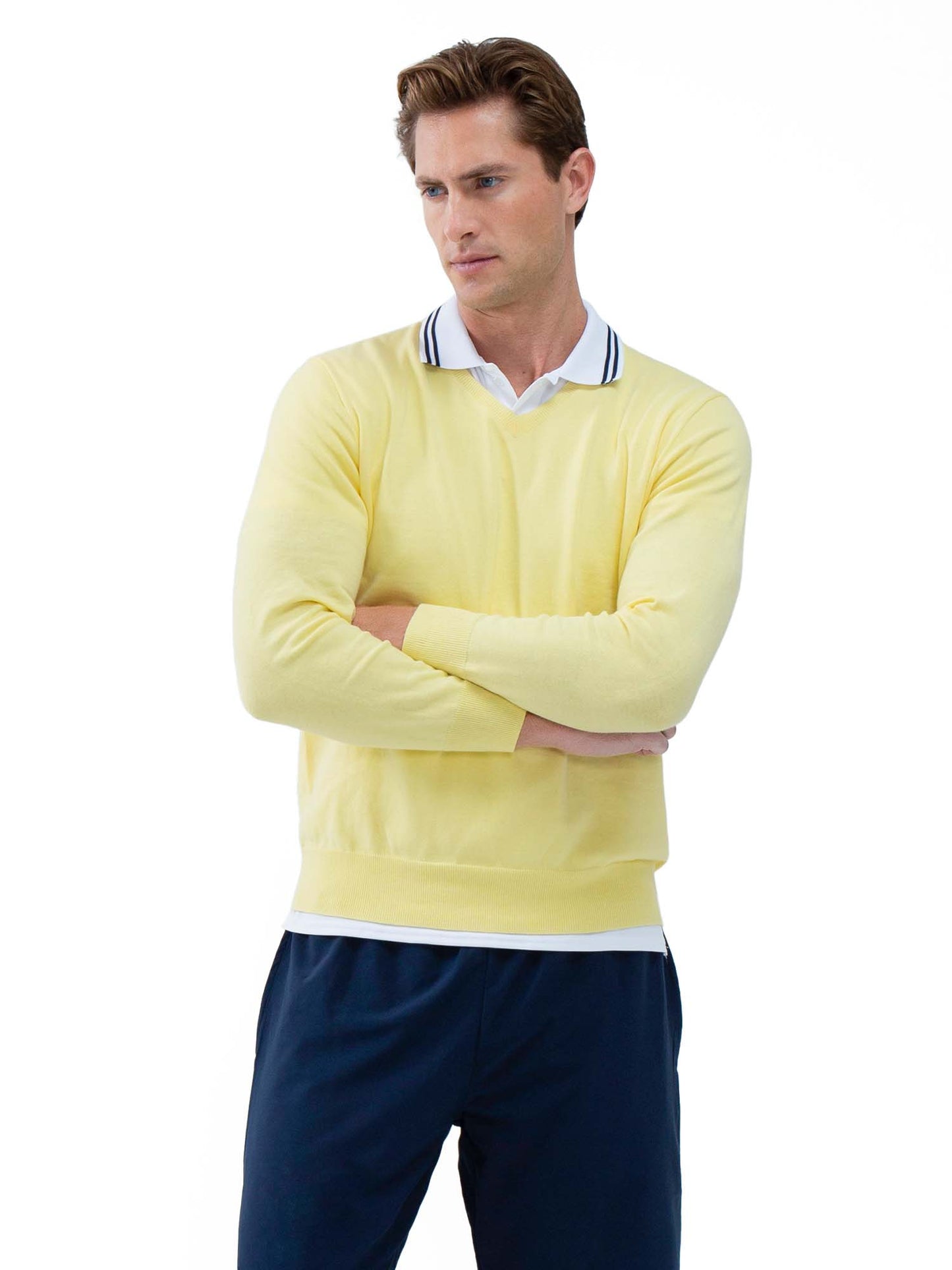 A man with light brown hair stands against a white background, arms crossed. He wears the inPhorm NYC Classic V Neck Sweater in Lemonade over a white collared shirt and dark navy pants, looking left with a neutral expression.