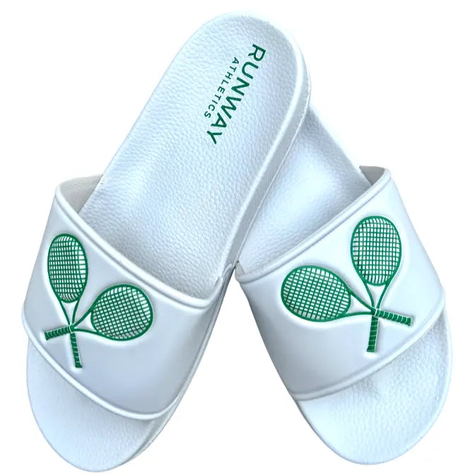 The Double Trouble Tennis Slides from Runway Athletics feature white straps with green tennis racket graphics. The right sandal’s insole is embossed with RUNWAY ATHLETICS in green, and the left sandal rests diagonally across the right one.