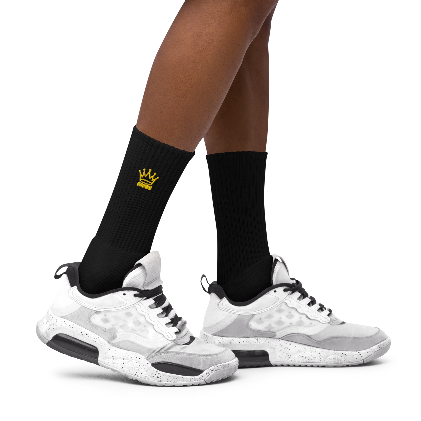 A close-up of a person wearing Crown Pickleball - Embroidered Logo Socks (Black) by Crown Pickleball, featuring a small yellow crown logo and cushioned sole, paired with white, grey, and black sneakers on a plain light grey background.