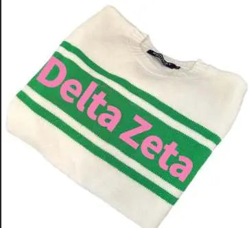 The Delta Zeta Tennis Sweater by Runway Athletics is a white crew neck with two green chest stripes and bold pink "Delta Zeta" lettering between them, plus a neatly visible collar tag at the top.