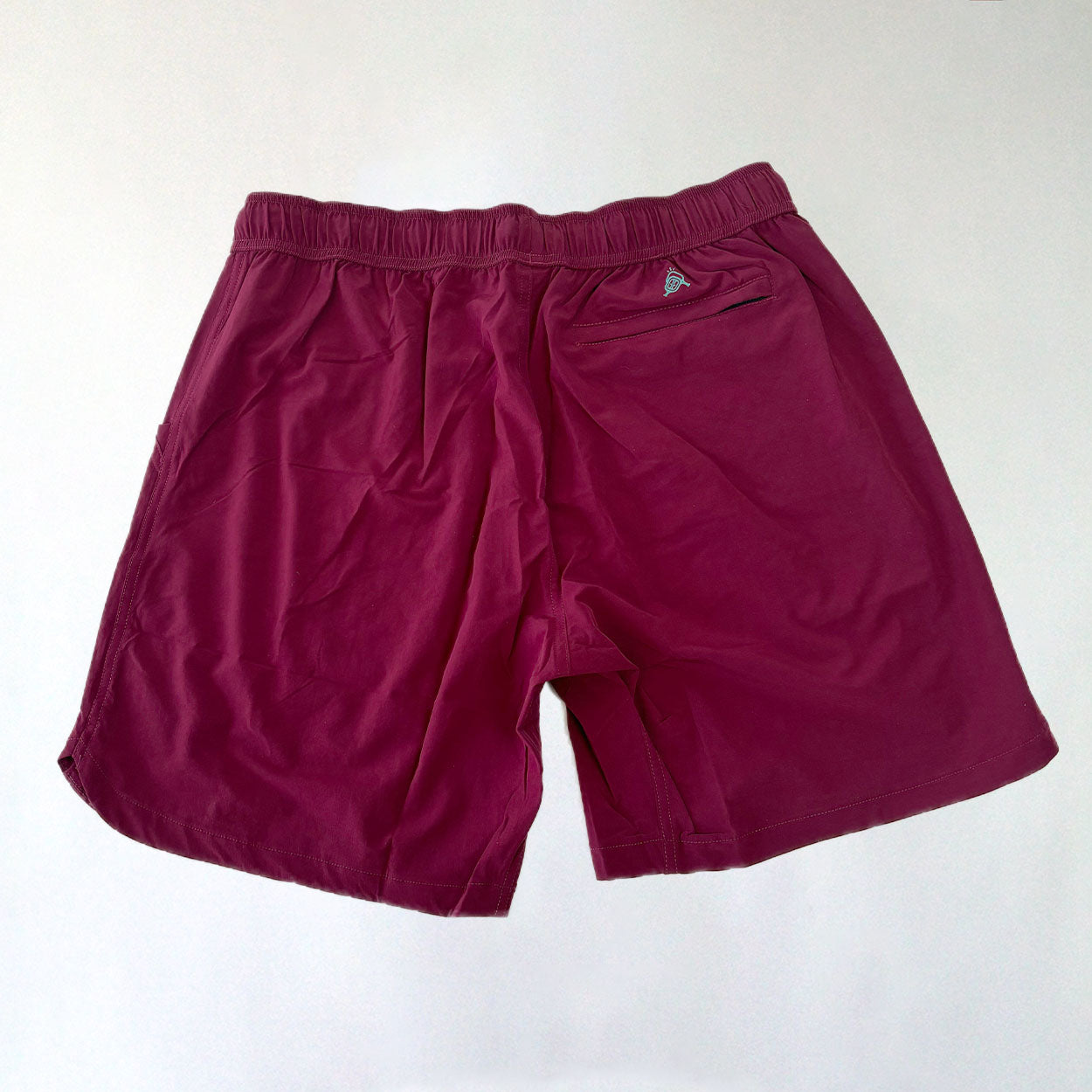 A pair of Good Get Magenta Me Crazy pickleball shorts without liner, featuring an elastic waistband and back pocket with a small colorful triangular logo, shown flat on a white surface. The soft fabric appears slightly wrinkled.