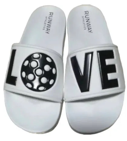 A pair of Pickleball Slides - White with Black by Runway Athletics. "RUNWAY GENESIS" is on the heels; the straps spell "LOVE," with the left sandal’s "O" as a black-and-white polka dot circle and "LVE" in bold black on the right.