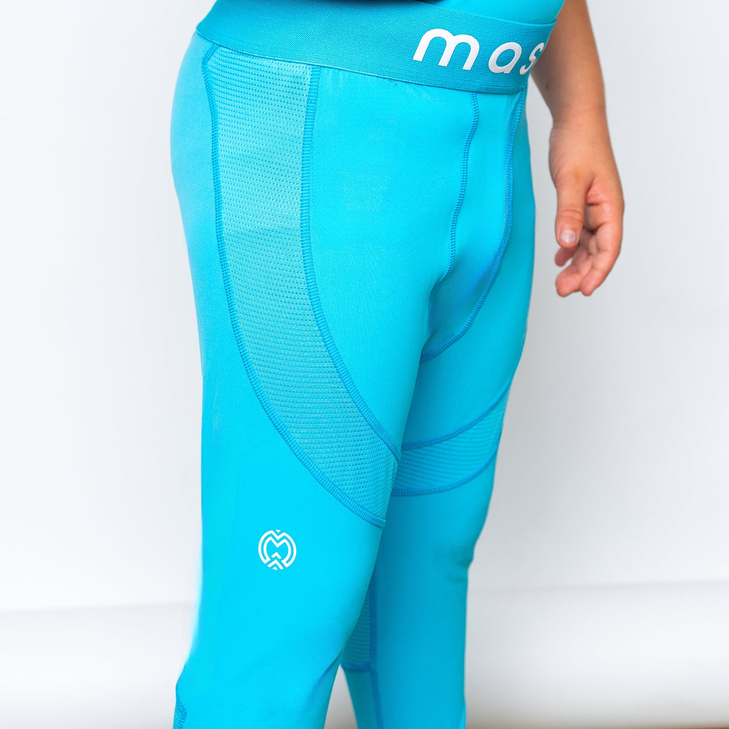 A youth boy wears Massov ProForm® Boys' Compression Pants in bright blue with mesh side panels and white logos near the waistband and knee. Only his lower torso, upper legs, and relaxed right arm are visible.