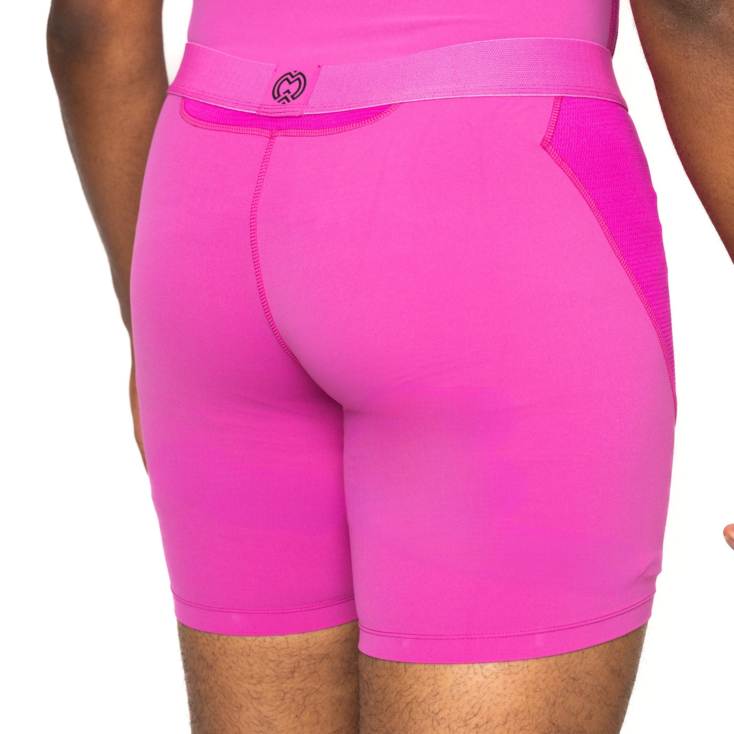 A person wears bright pink Massov ProForm® Men’s 7″ Compression Shorts with a wide waistband and visible stitching. The photo, against a white background, shows their lower back, thighs, and part of their arm at the side.