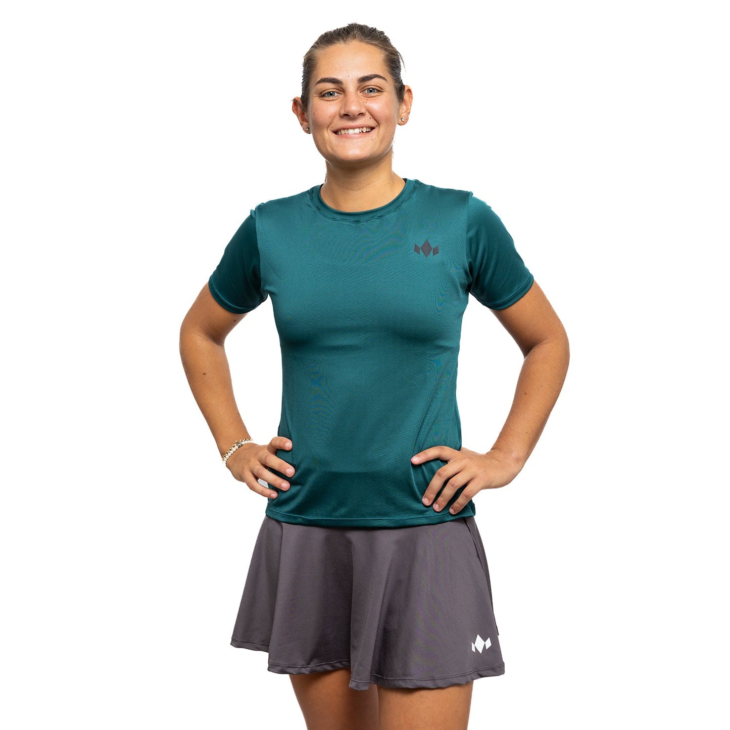 A smiling woman with her hair tied back wears the Diadem Sports Team Women's Essential Crewneck in teal and a gray tennis skirt, posing against a white background with her left hand on her hip. She also accessorizes with a bracelet.