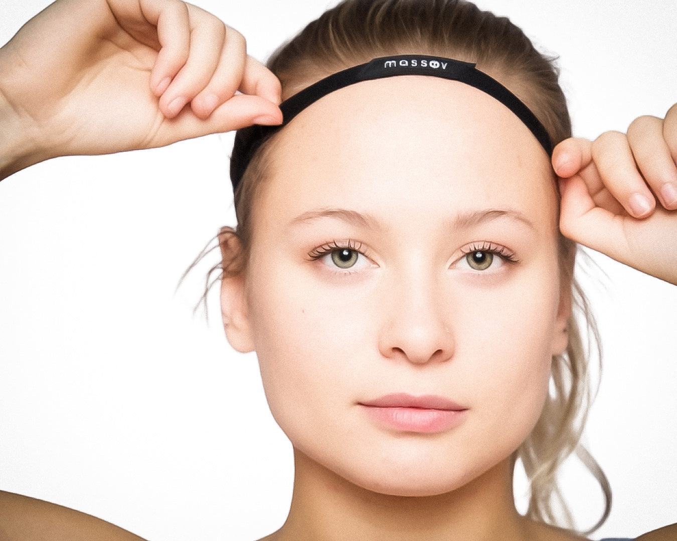 A young woman with fair skin and light eyes, hair pulled back, wears the Massov Thin Sports Headband in black across her forehead. She faces the camera with a neutral expression against a plain white background.