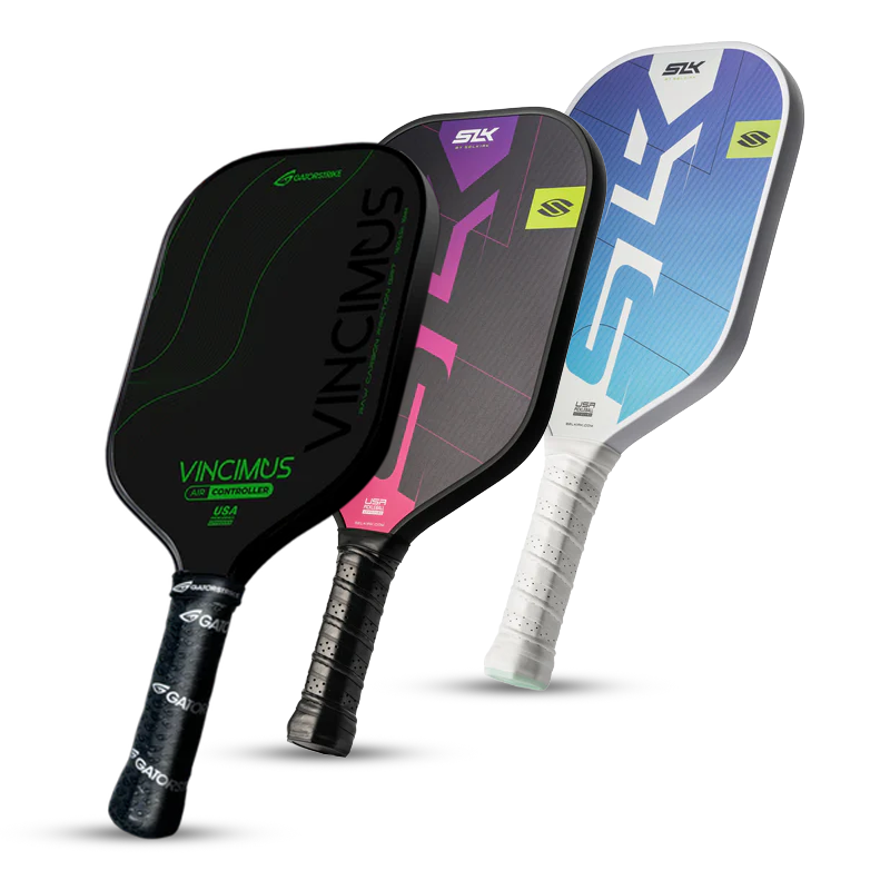 Three pickleball paddles stand upright, overlapping. The first is black with green accents and “VINCIMUS” text, the second is black with pink details, and the third is white with blue and gray accents.