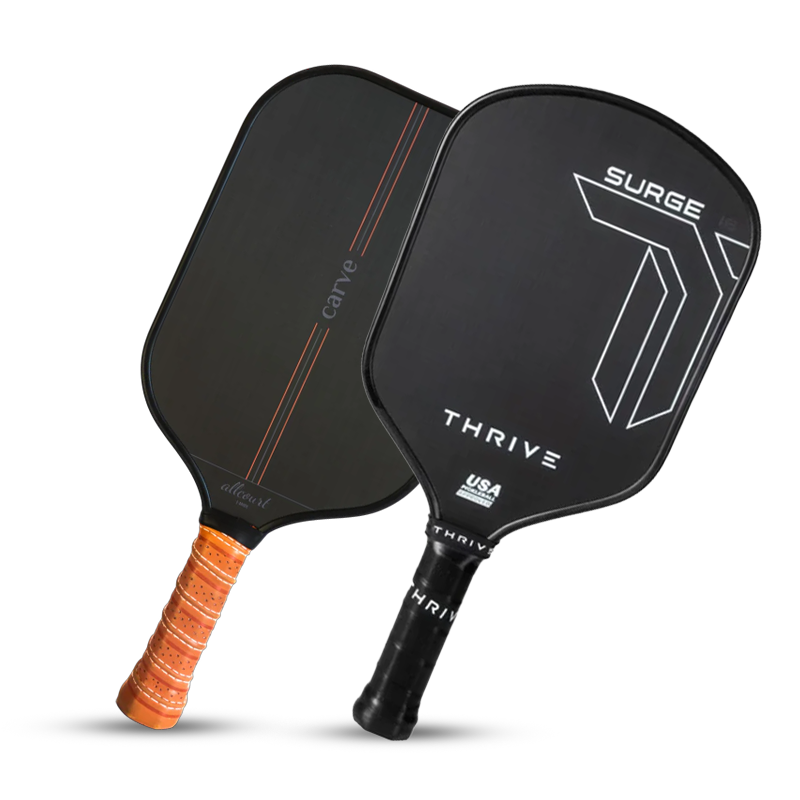 Two pickleball paddles stand upright side by side. The left paddle has a brown grip and sleek black face with an orange accent; the right paddle has a black grip and bold white graphics reading “SURGE” and “THRIVE.”.