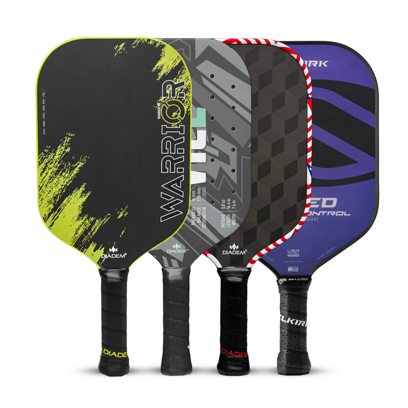 Four pickleball paddles stand upright side by side. Each has a unique design: black/yellow Warrior, gray/black geometric, blue/black with red trim, and a blue/black paddle with white accents.