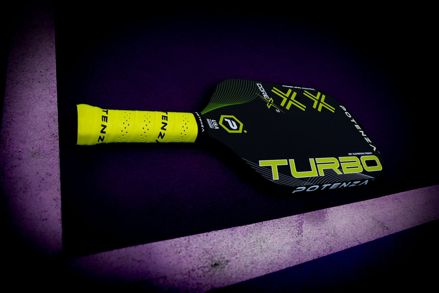 A black Potenza Pickleball TURBO+ COREx2 paddle with a yellow grip and bright accents, built for power play, rests on a purple court near a white line. Diagonal yellow lines and branding highlight its carbon fiber face.