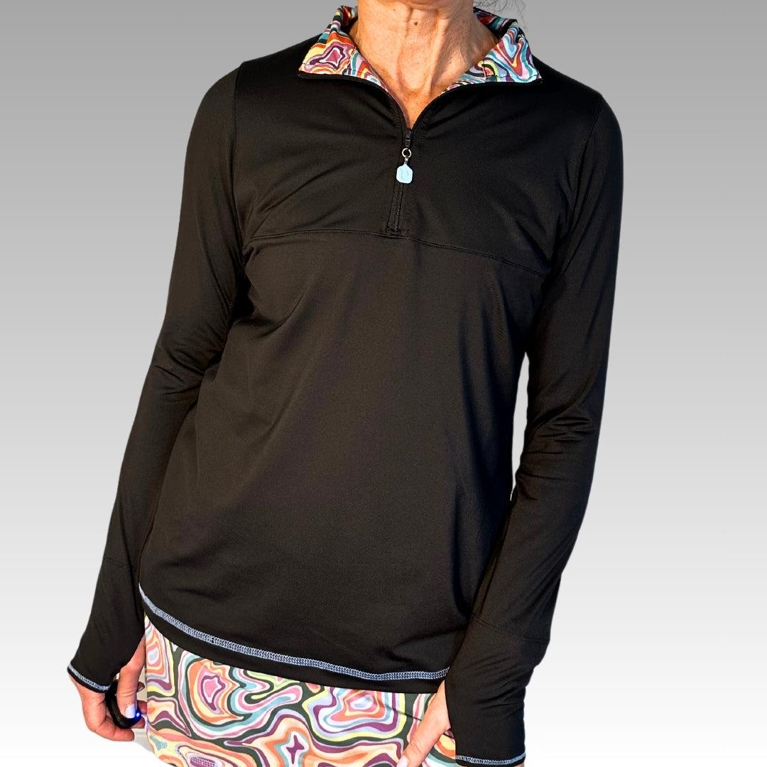 A person wears the Playly Store Soleil Tech Shirt with a half-zip collar and colorful lining, paired with bold swirl shorts. Both are made from breathable, UV-protective fabric. The scene has a light gray gradient background.