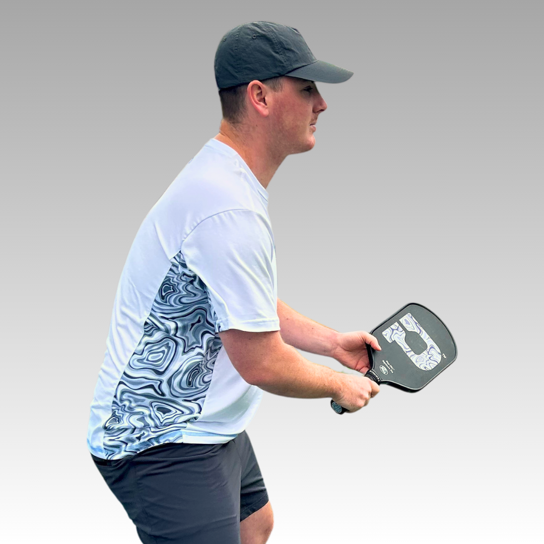 A man holding a paddle and wearing the Playly Store Warrior Tee 2.0, a top moisture-wicking t-shirt perfect for pickleball fans.