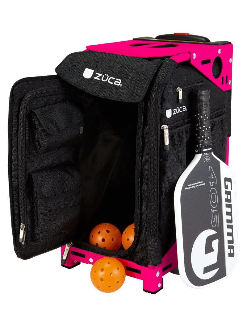 A vibrant pink ZUCA Pickleball Pro Black/Black rolling bag sits with its front pocket open, revealing mesh inner pockets and three orange balls. A black and white paddle is stored in the side pocket, ideal for organized pickleball gear storage.